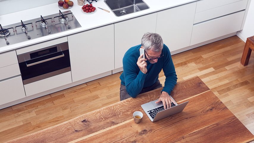 Mand sidder i køkken med telefon og computer