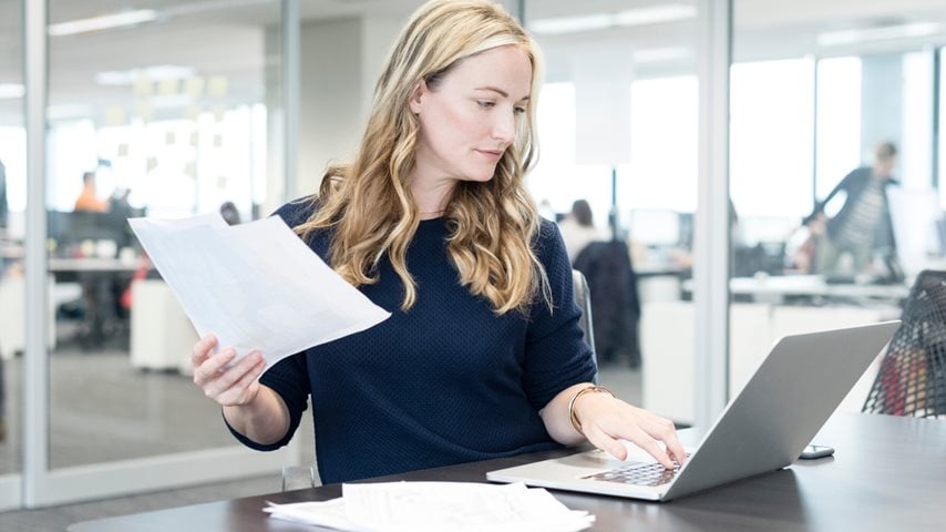 Kvinde sidder i mødelokale med papirer og computer