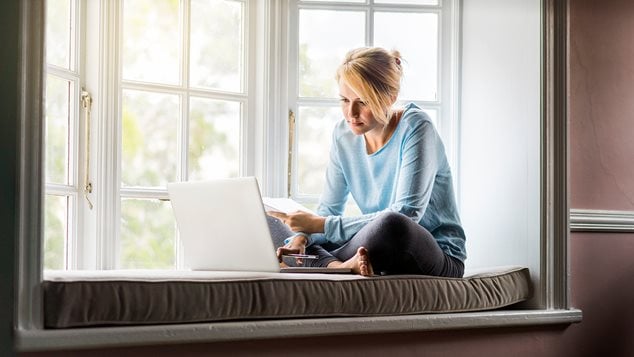 Kvinde sidder i vindueskarm og kigger på sin computer