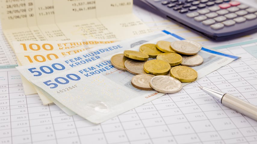 Pengesedler og mønter ligger på papir ved siden af en lommeregner